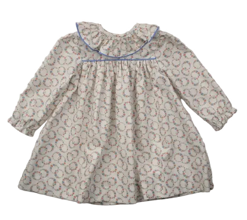 A long-sleeve baby dress with a beige and gray floral pattern, featuring a ruffled collar trimmed with blue piping, laid flat on a white background.