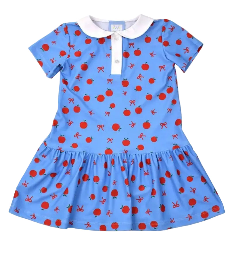 A light blue short-sleeve dress for toddlers or girls, featuring an all-over red apple and bow pattern, a white collar, and a white button placket. It is displayed flat on a white background with a brand tag and a hangtag attached.